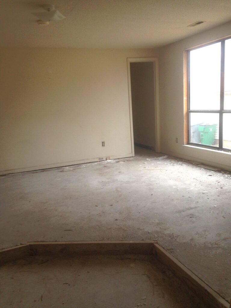 Empty room in a distressed property with carpet removed down to the subfloor during renovation.
